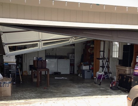 Image of crooked garage door hanging after cables have come off.