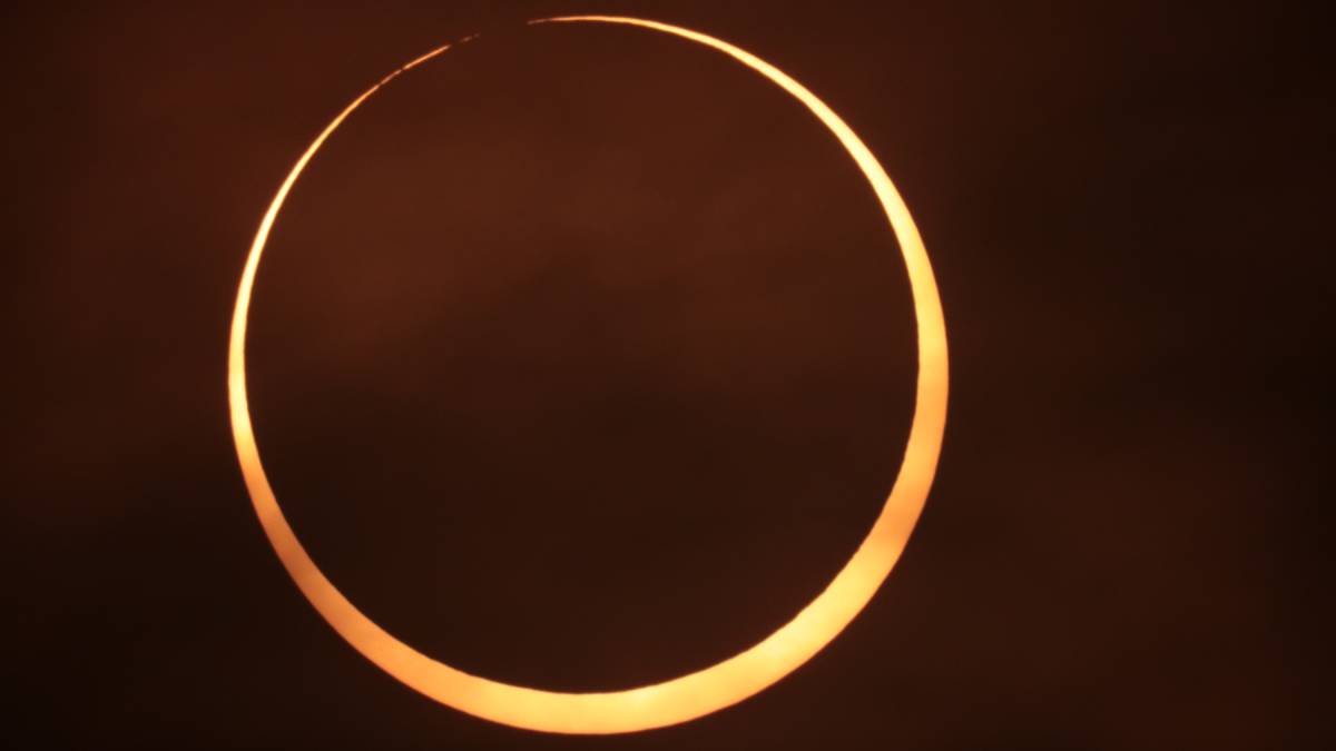 A ring of fire annular solar eclipse just before maximum eclipse on a burnt orange sky.