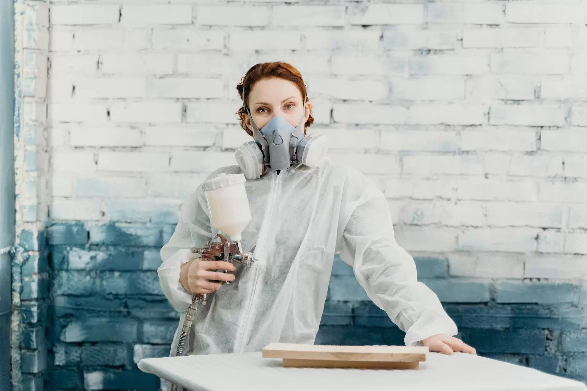 a woman wearing personal protective equipment leaning on a table while looking at the camera
