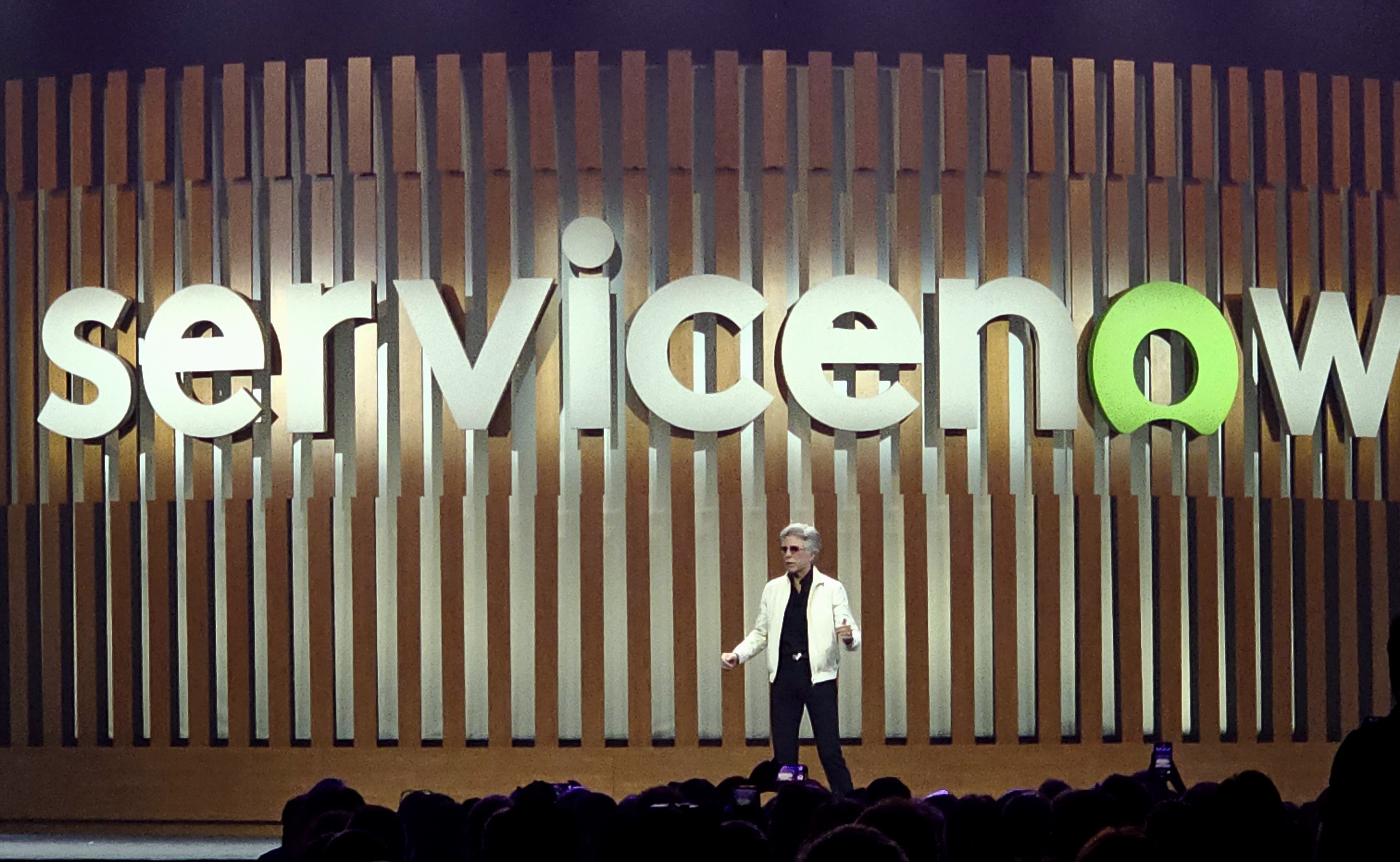 ServiceNow CEO on stage with the large ServiceNow logo behind him during a company event.