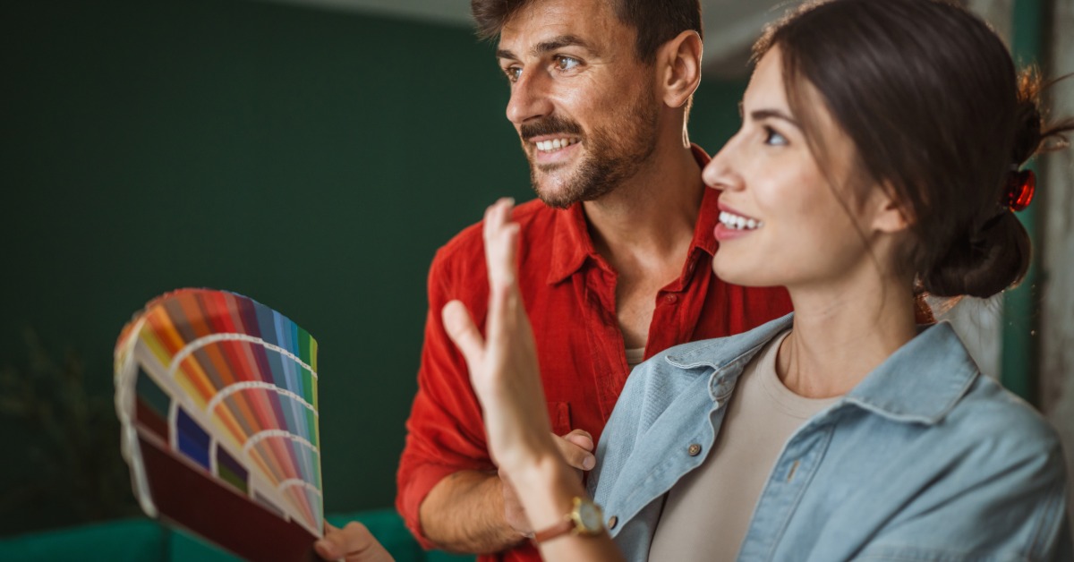 A man and a woman standing together in a room, using a large stack of paint swatches to choose a new color for the room.