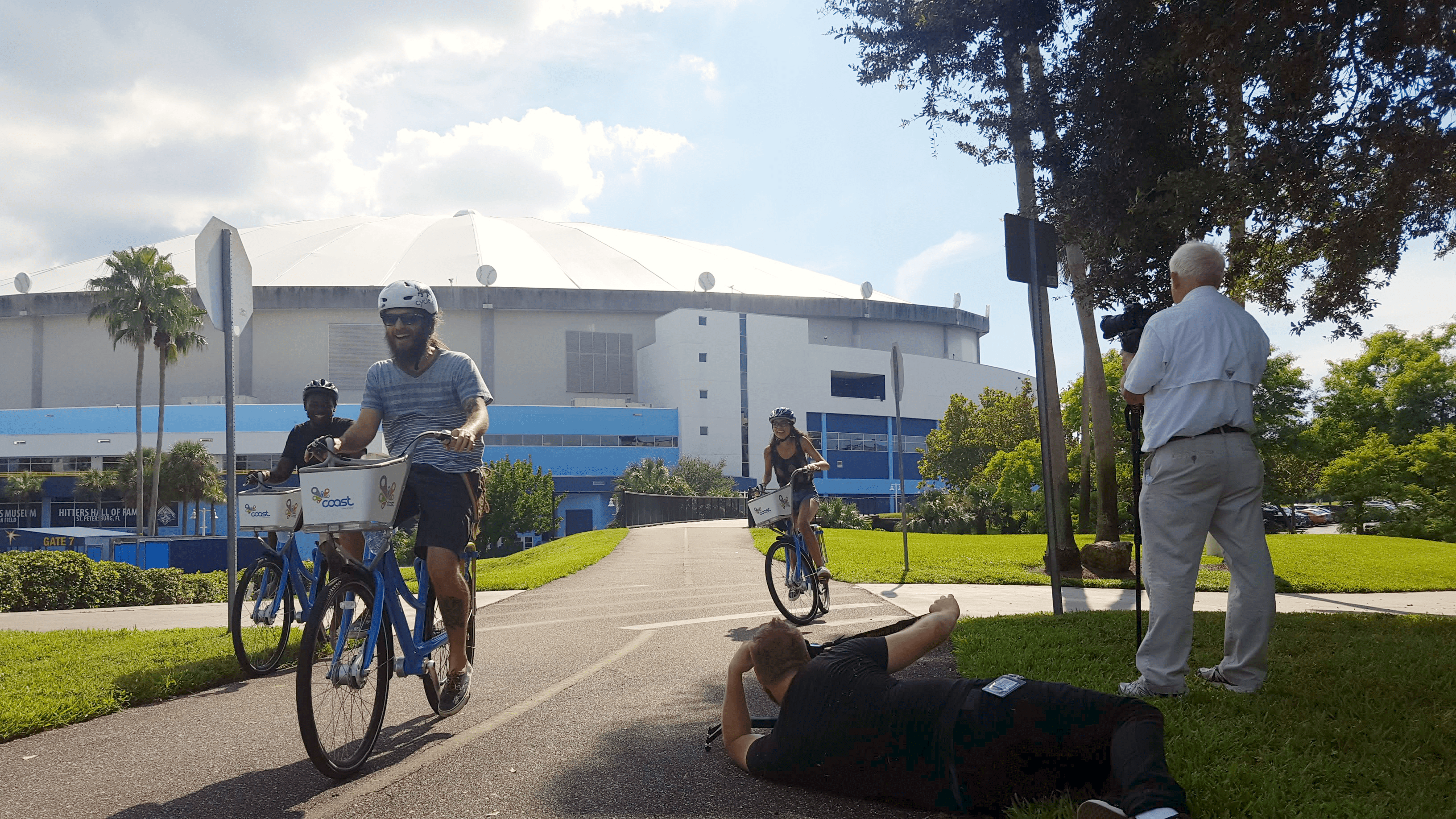Three cyclists ride by a camera crew while shooting the Coast St. Pete preview video.