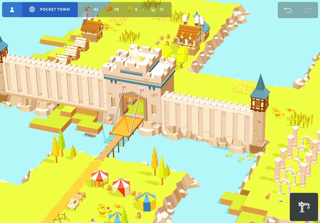 Captura de pantalla de Pocket Build. Vista de pájaro de parte del pueblo, con un campamento de tiendas de campaña y las murallas de un castillo. Escena con suelo verde y rio azul.