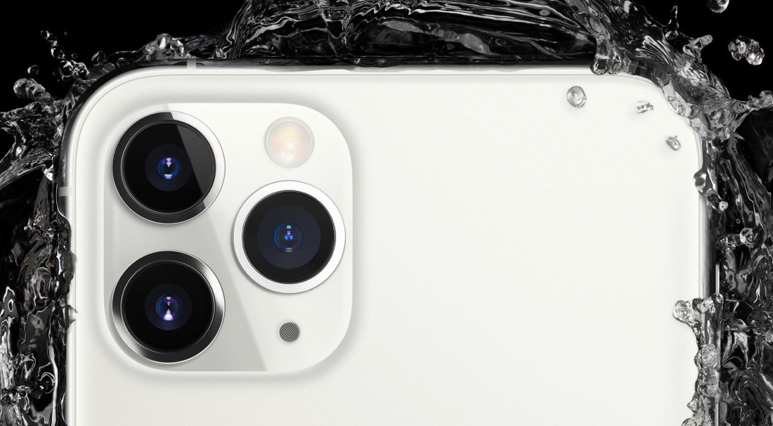 Parte trasera superior del iPhone 11 Pro. Se ven las tres lentes de la cámara y una gran salpicadura de agua en la parte posterior.