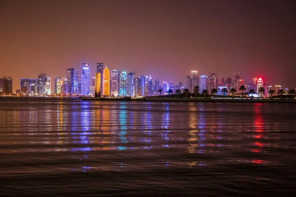 Skyline nocturno de Doha: rascacielos iluminados y reflejos en el mar, una postal imperdible durante una escala de crucero.