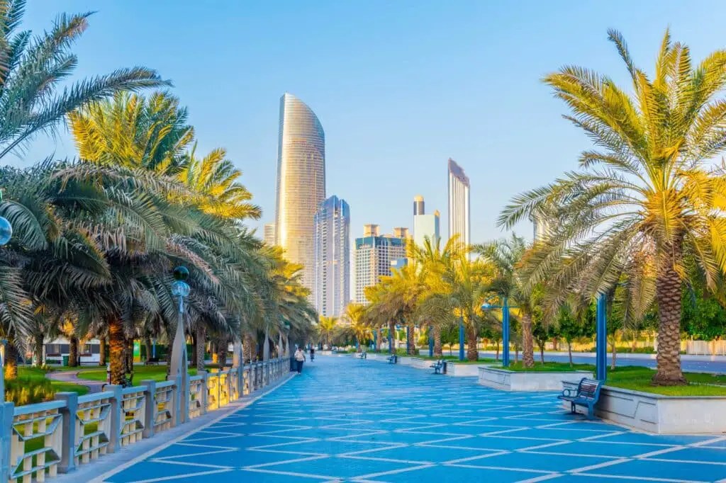 Vista del paseo marítimo de la Corniche en Abu Dhabi, con su sendero azul rodeado de palmeras, ideal para caminar con tranquilidad y disfrutar del skyline moderno de la ciudad durante una escala de crucero.