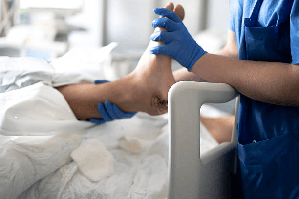 Nurse wearing blue gloves performing wound care on a patient's foot in a hospital bed