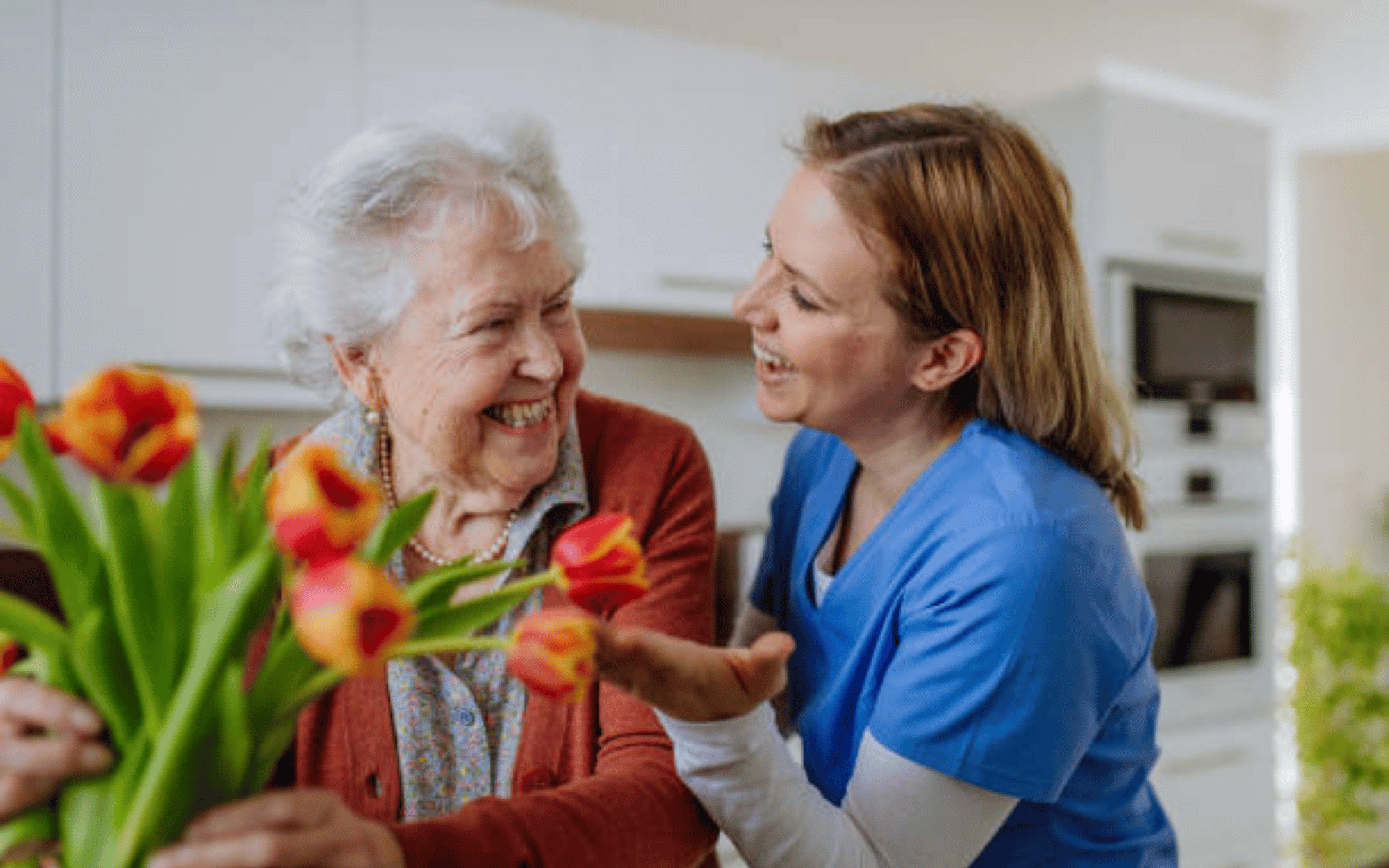 A family caregiver taking care of an older women in her home in the spring looking at beautiful orange and red flowers. 