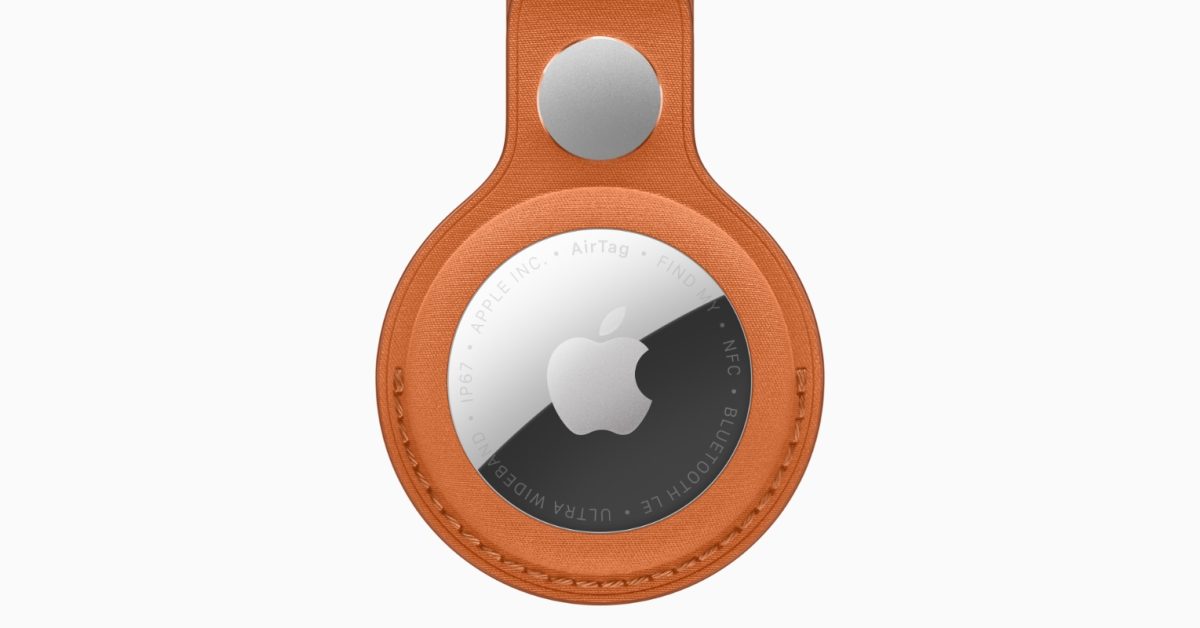 An Apple AirTag with a silver logo is secured inside an orange leather key ring holder.