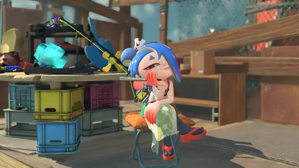 A blue-haired character from Splatoon relaxes on a folding chair next to a table with fishing gear.
