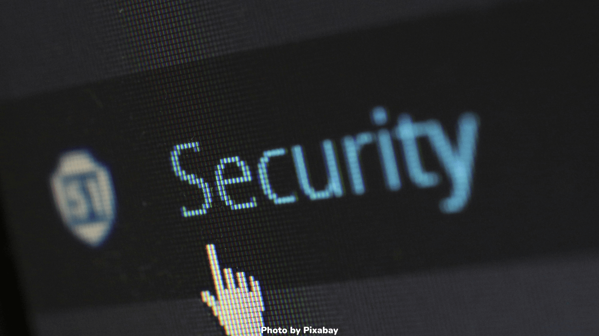 A close-up of a computer screen displaying the word Security with a cursor pointing at it. The image has a pixelated texture, and a shield icon is visible to the left of the text.
