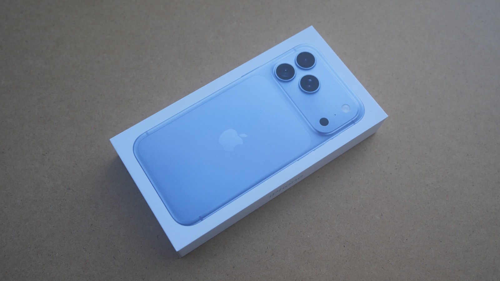 A light blue smartphone in a white box, displaying the Apple logo and the back design with a dual-camera setup.