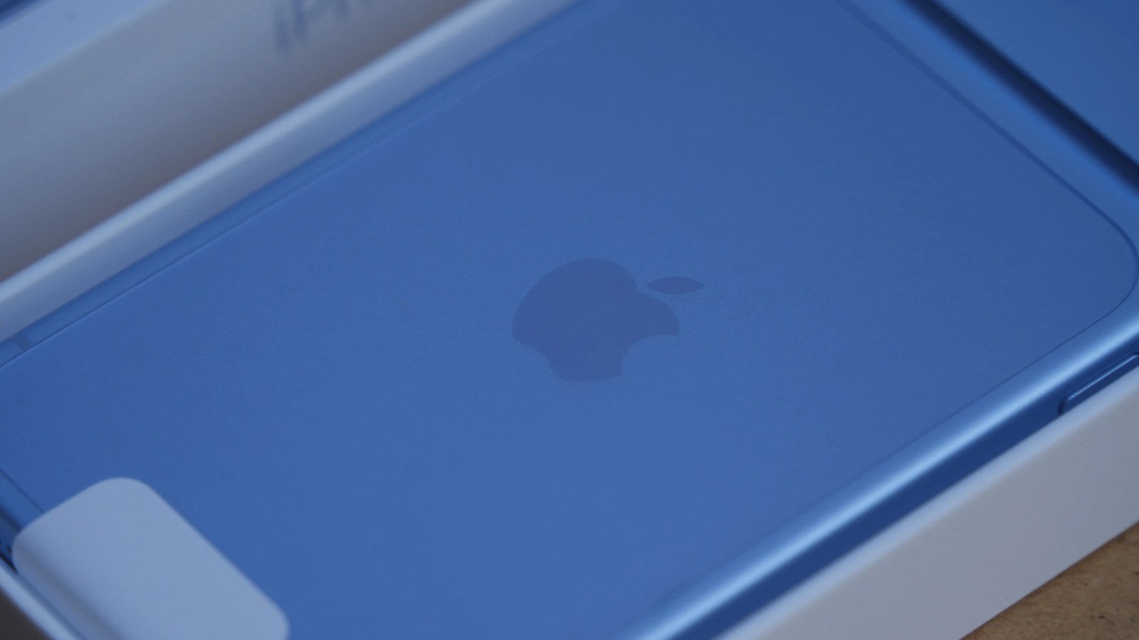 Close-up of a blue iPhone box featuring the Apple logo inside an unboxing setting.