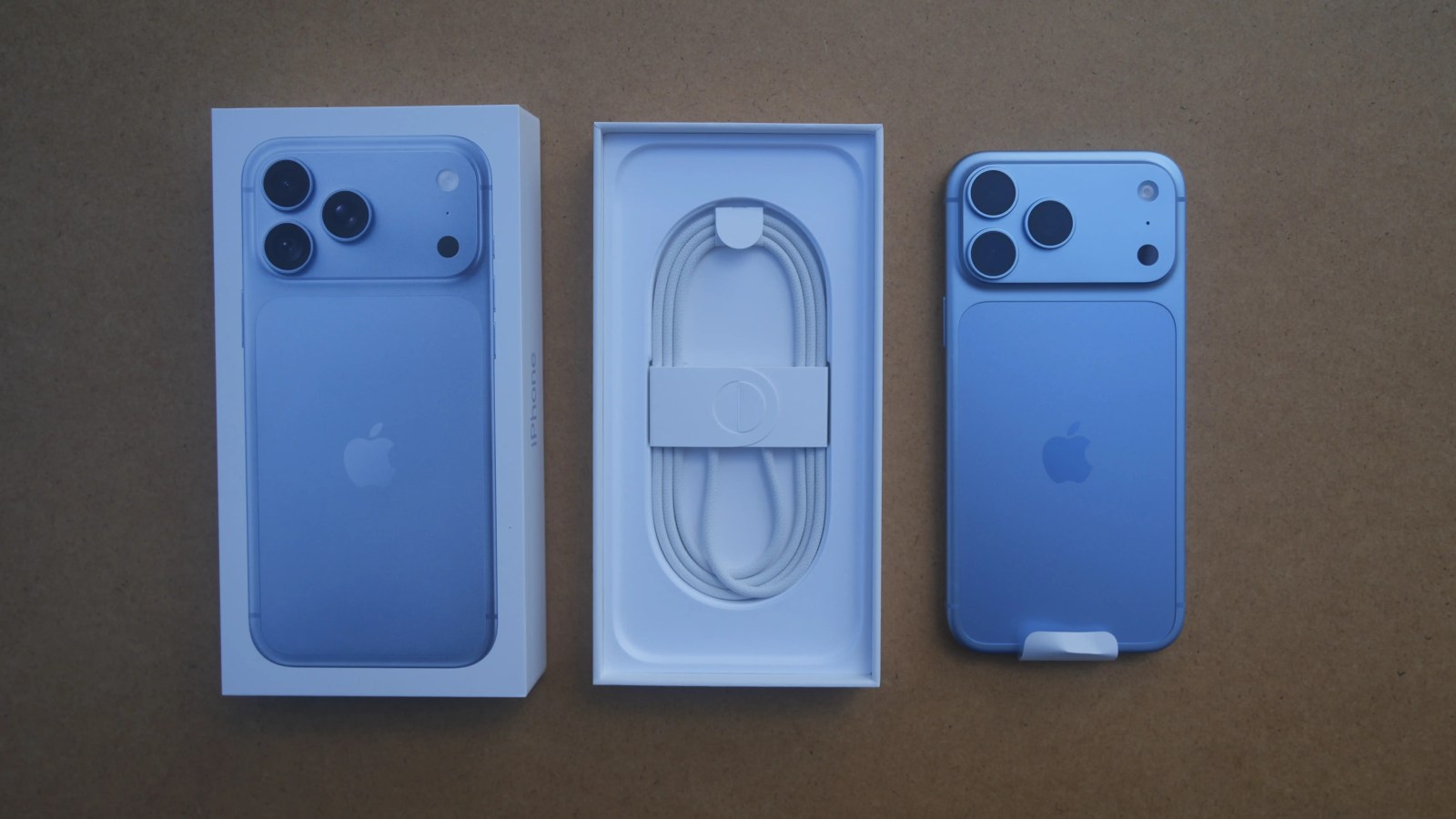 A blue iPhone lies next to its open white box containing a coiled charging cable.