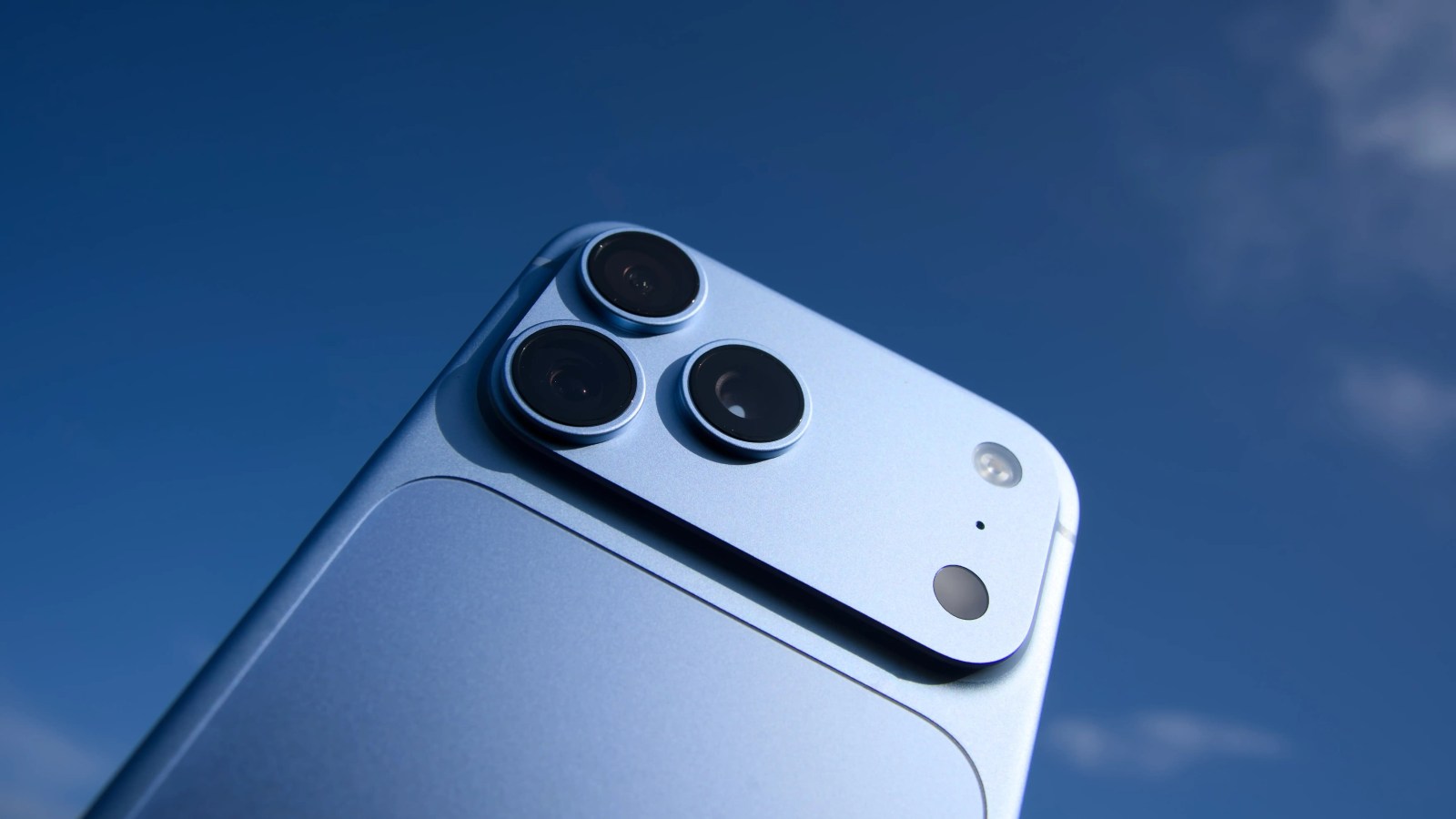 A light blue smartphone is angled upward against a clear blue sky.