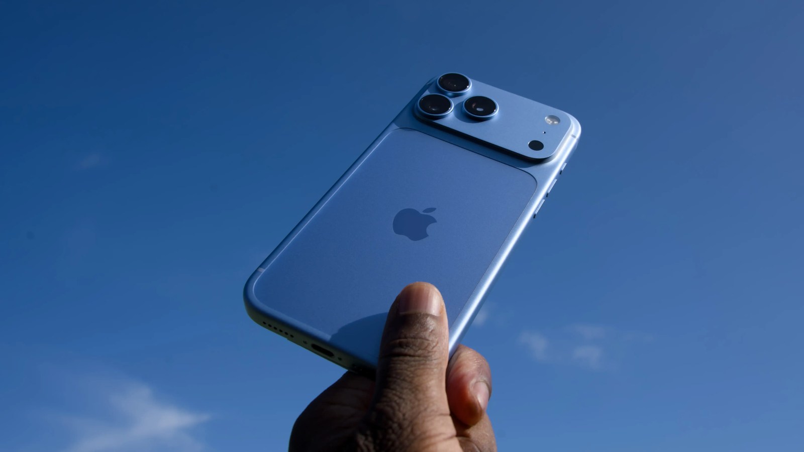 A hand holding a blue smartphone against a clear blue sky.