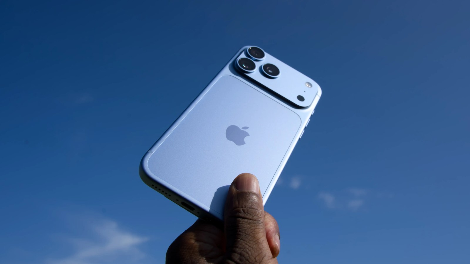 Close-up of a hand holding a light blue smartphone against a clear blue sky.