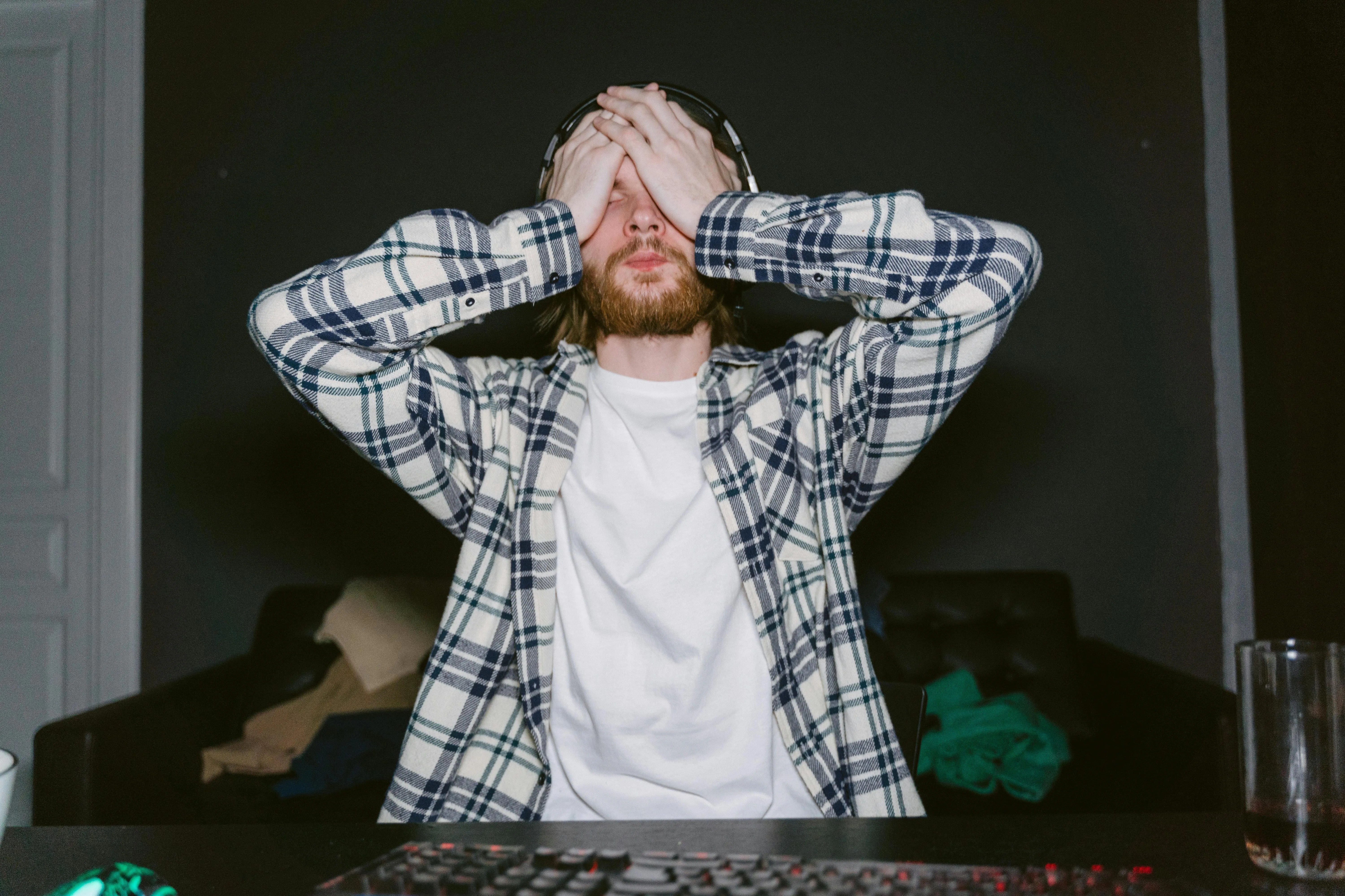 A frustrated man sits at his computer with his hands covering his face in disappointment.