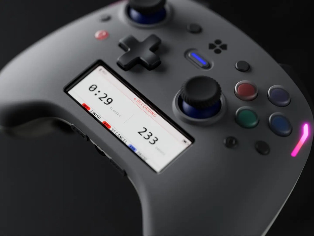 A grey game controller features a built-in screen displaying a recording timer and various control buttons.