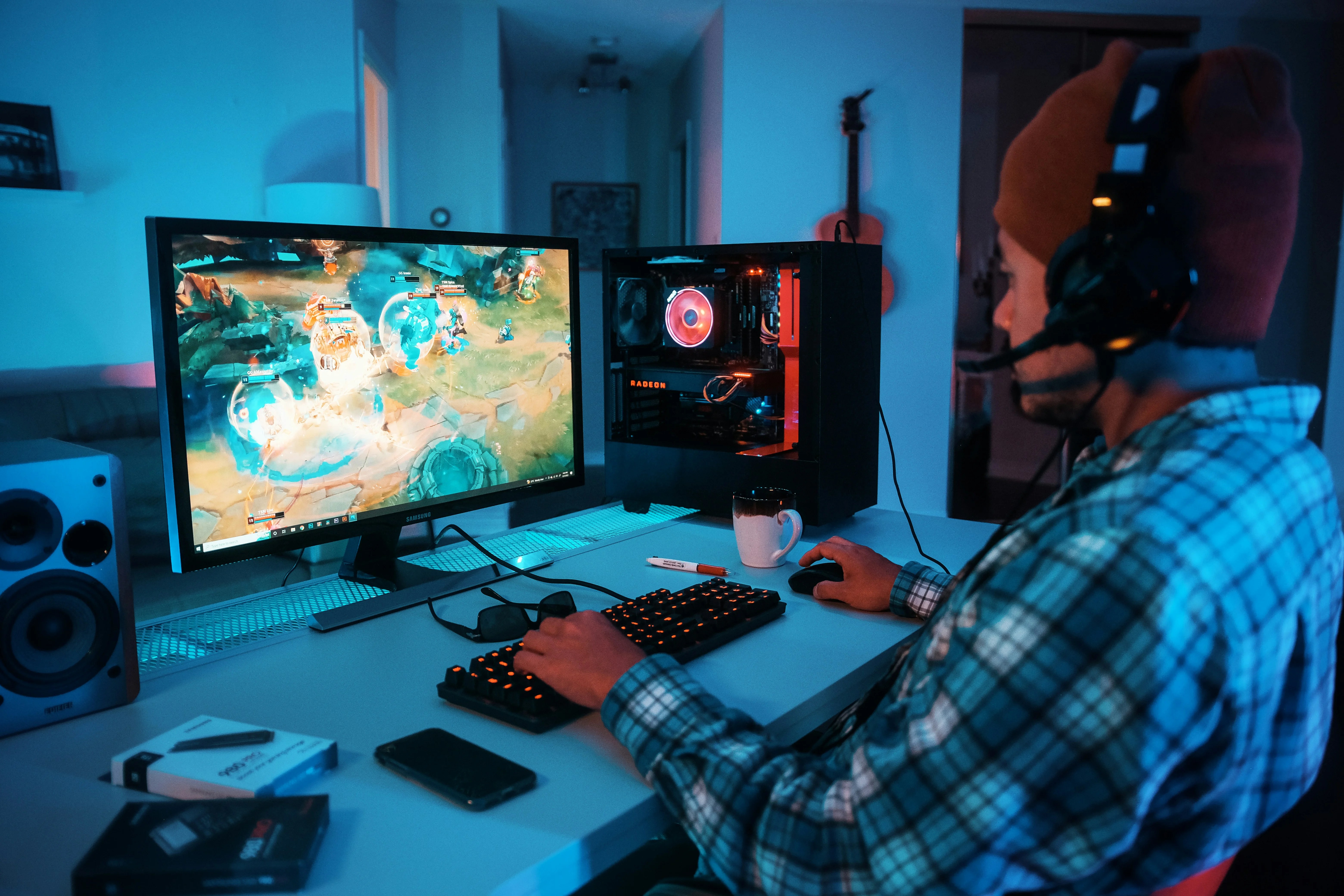 A gamer wearing a headset plays a video game on a PC with blue ambient lighting.