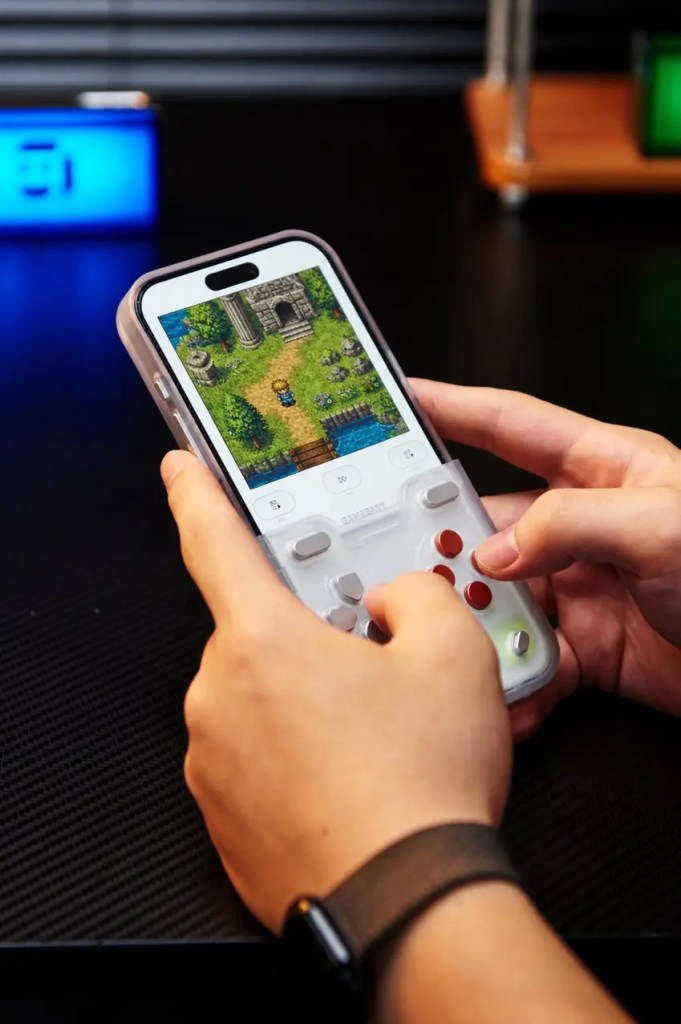 Hands holding a smartphone equipped with a GameBaby physical controller case to play a retro-style game.