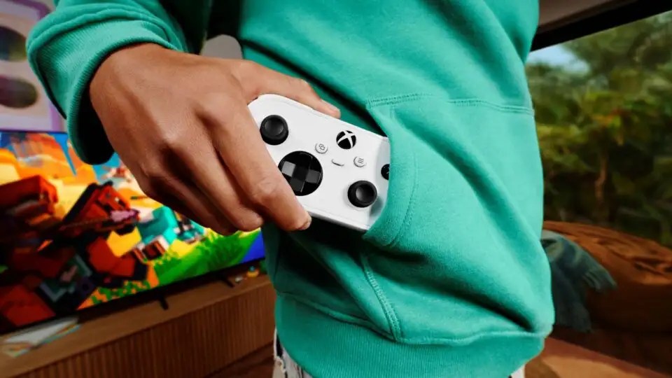 A person wearing a green hoodie slides a white Xbox controller into the front pocket.