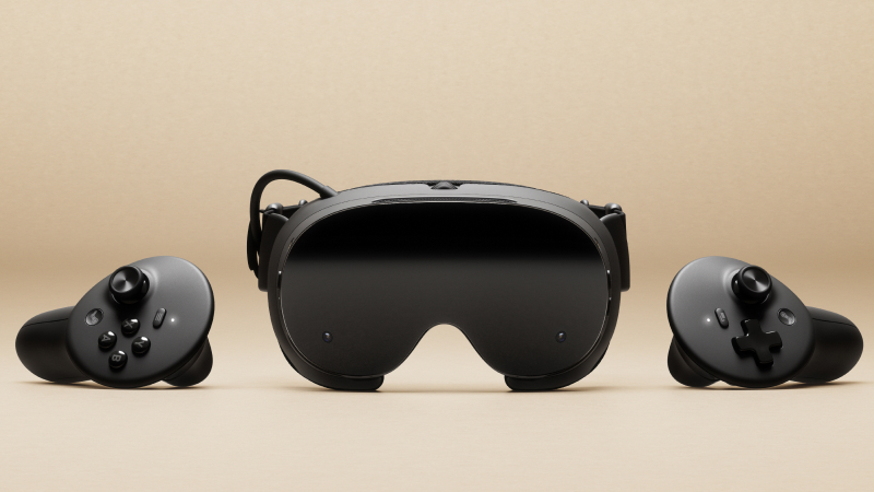 A black virtual reality headset sits centered between two matching handheld controllers on a beige background.