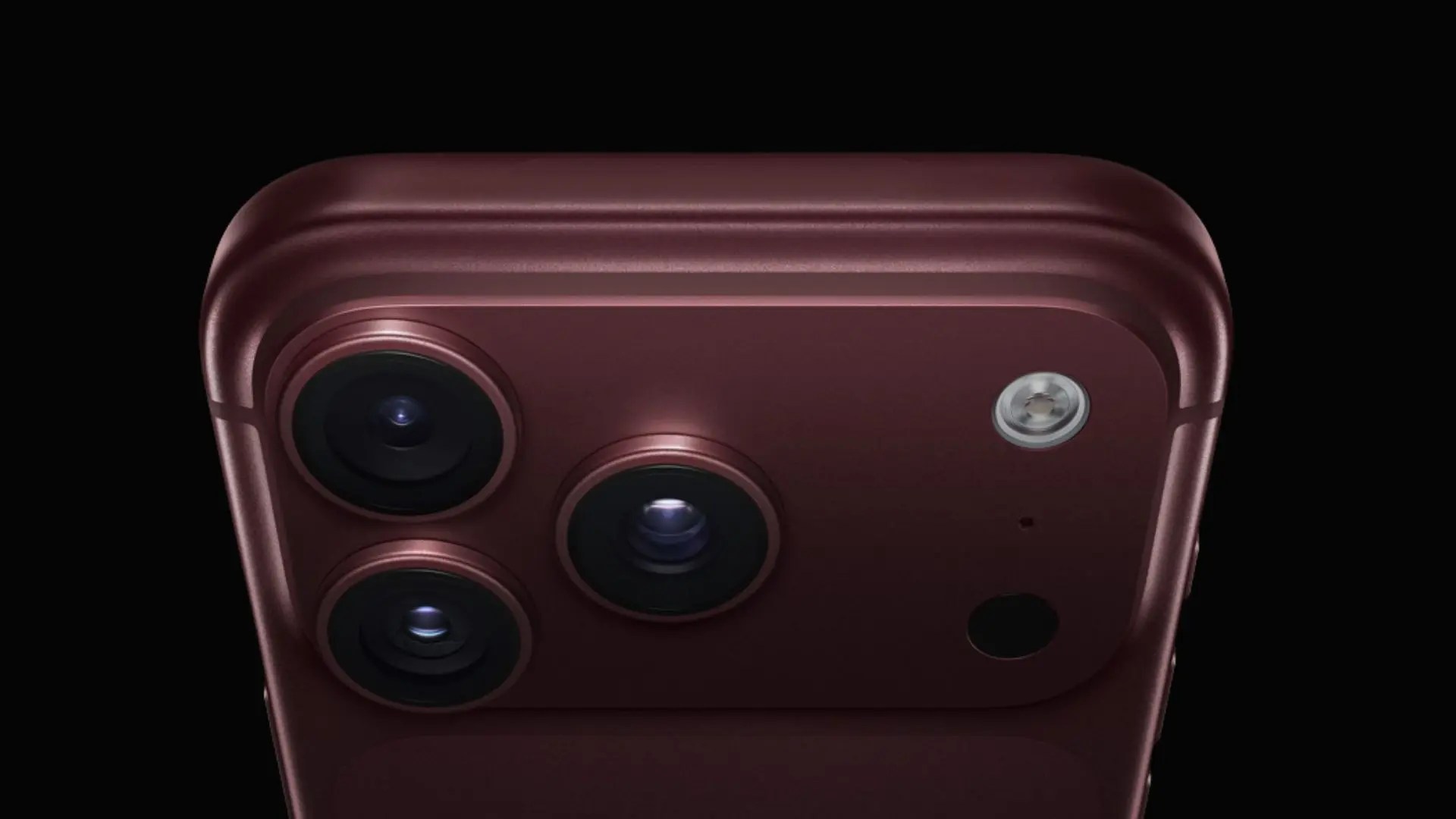 Close-up of a burgundy smartphone showing its triple-camera system, flash, and sensor against a black background.