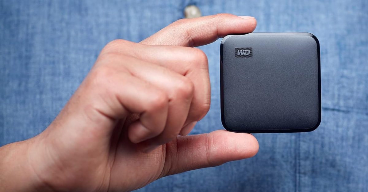 A hand holds a small, square WD Elements SE portable SSD against a blue denim background.