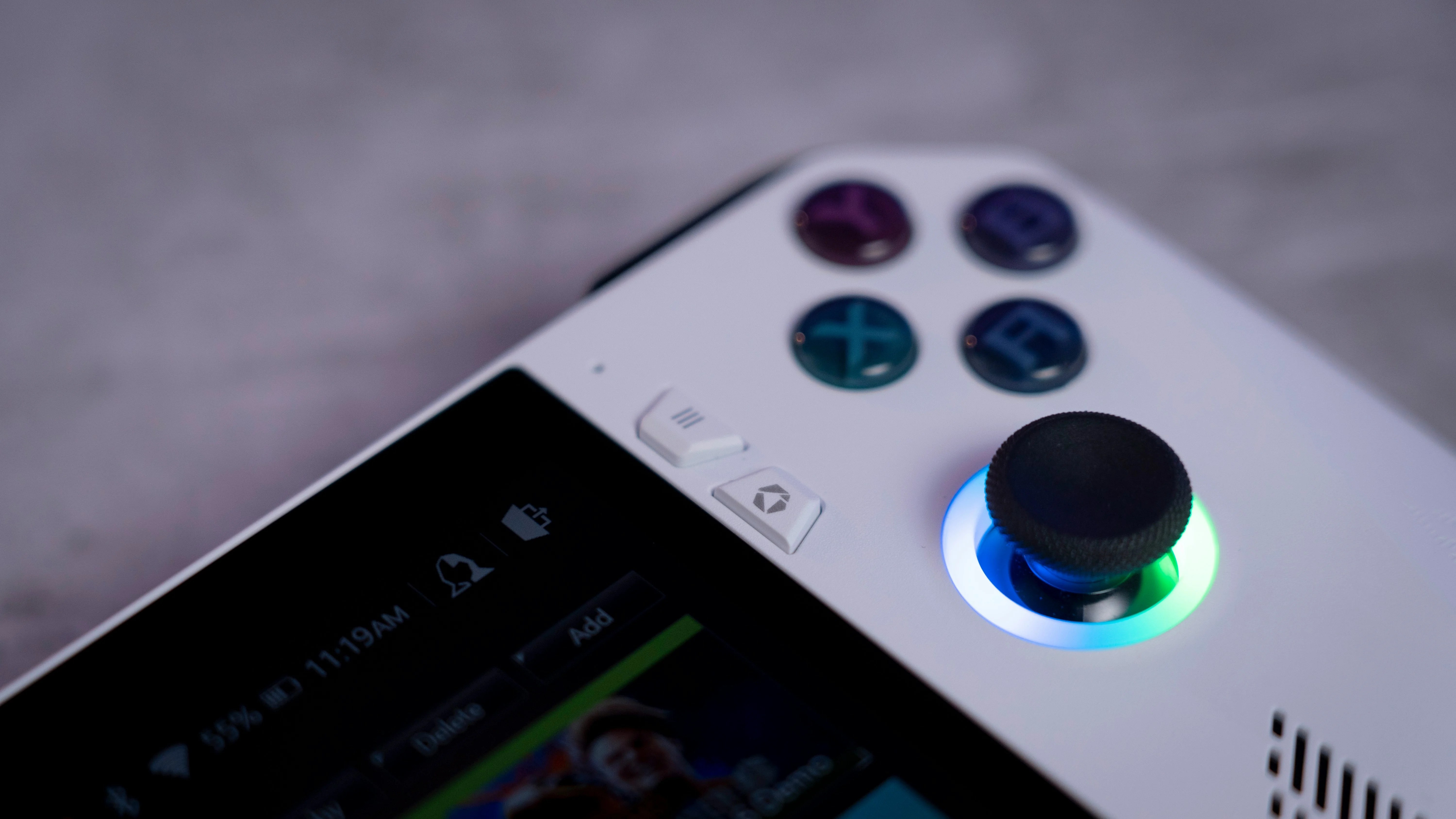 A close-up of a white handheld gaming console featuring a glowing joystick, action buttons, and a screen.