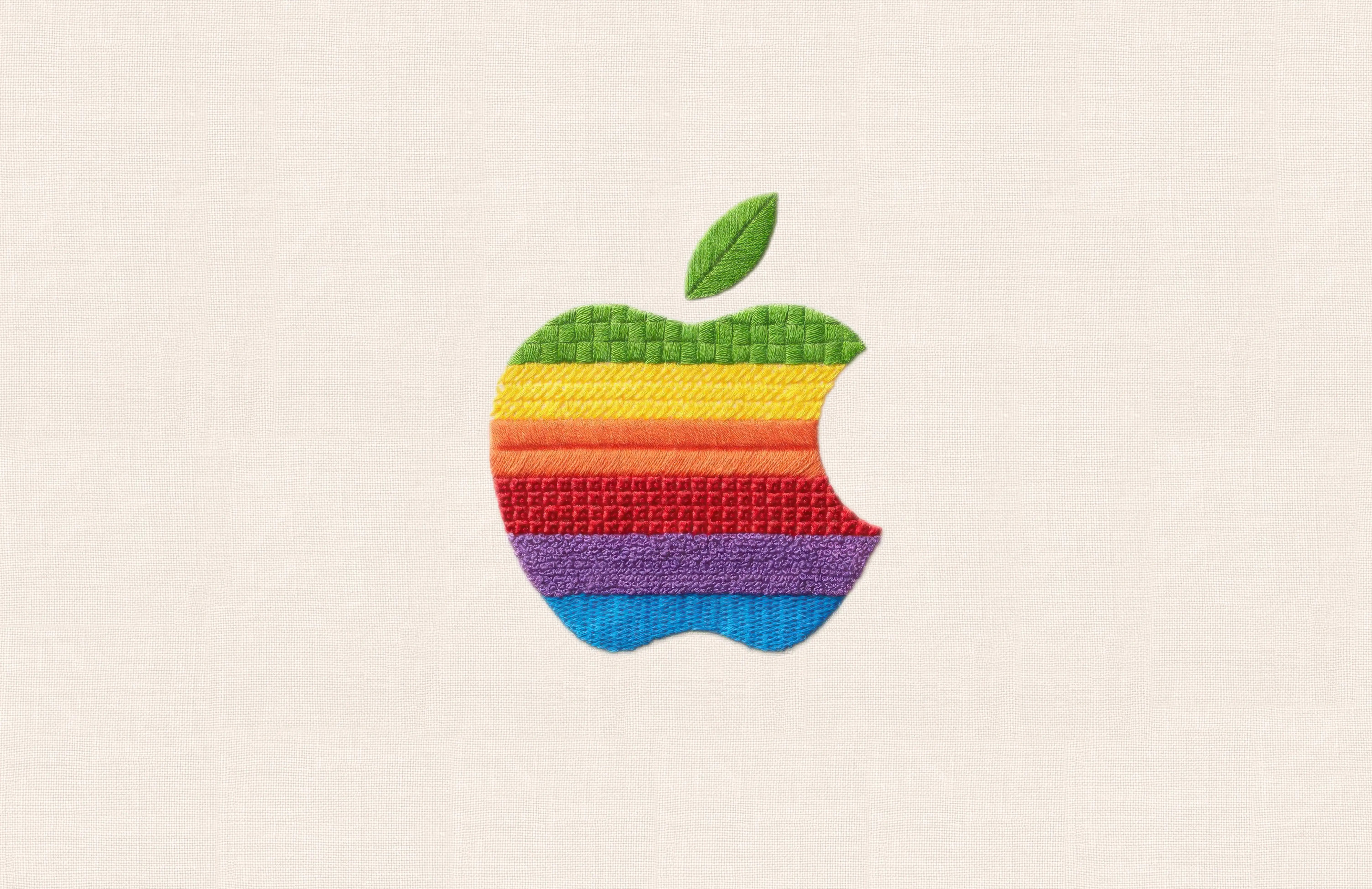 Embroidered rainbow Apple logo with a textured green leaf against a neutral fabric background.