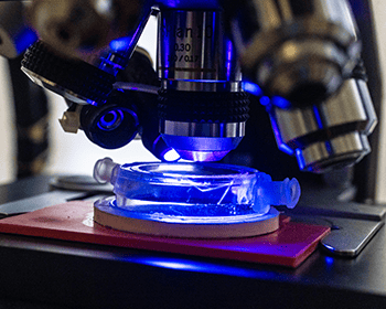 Close-up view of a microscope focusing on a glass slide illuminated by blue light.