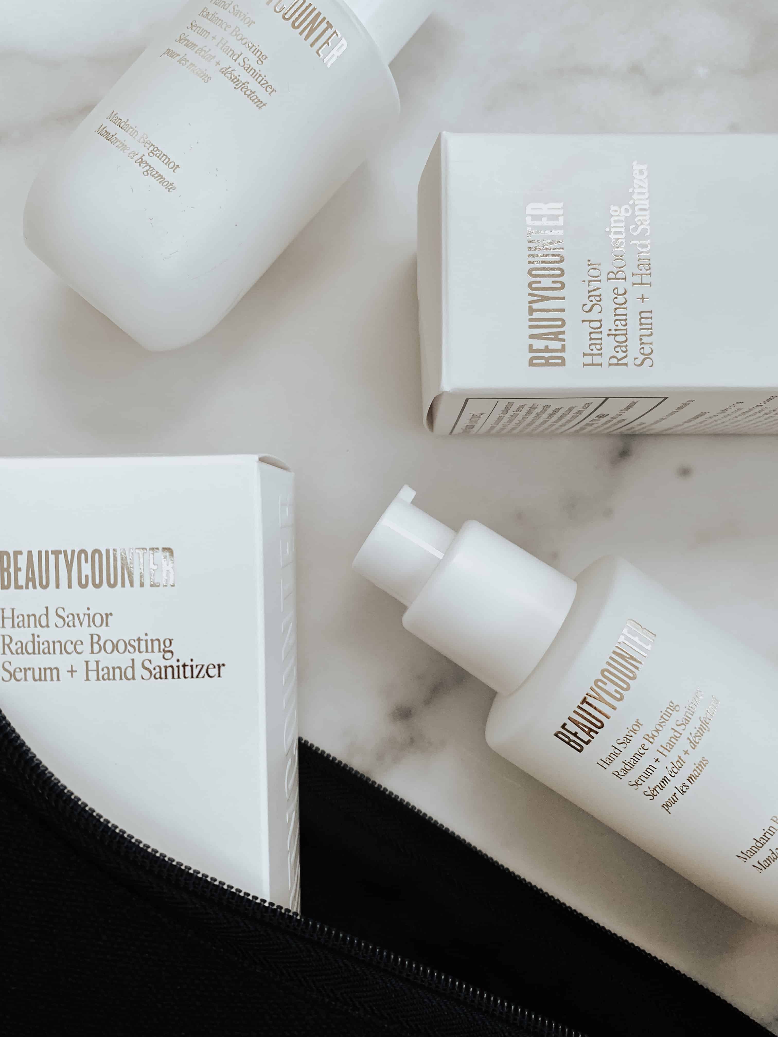 Two sets of Beautycounter's new Hand Savior Radiance Serum + Hand Sanitizer bottle and product packaging on a marble surface.