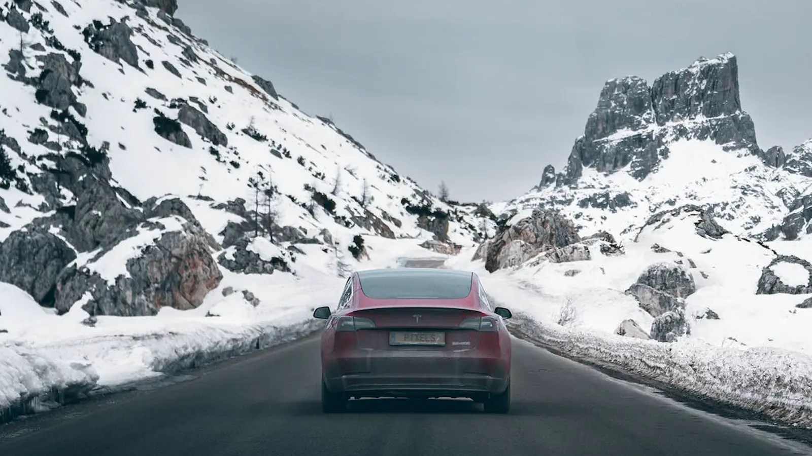tesla ev driving through mountains in snow