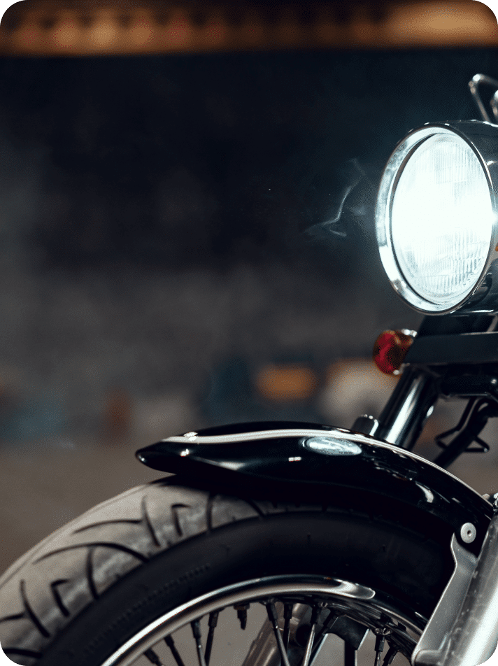 Vue rapprochée sur la roue avant et le phare d’une moto noire. Close-up of the front wheel and headlight of a black motorcycle.