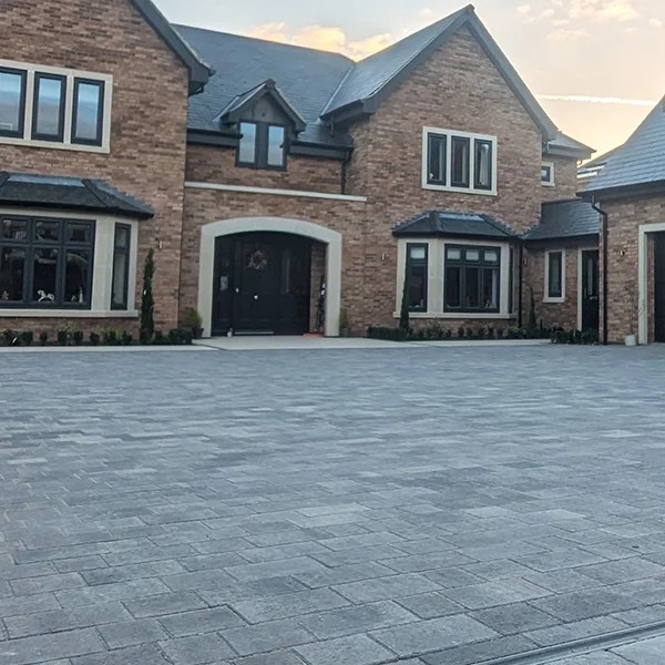 The front view of a large brick built house featuring a grey block paved driveway