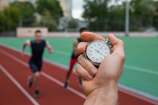 Picture of young athletic men run on running track outdoors. Historic stop watch time measurement.