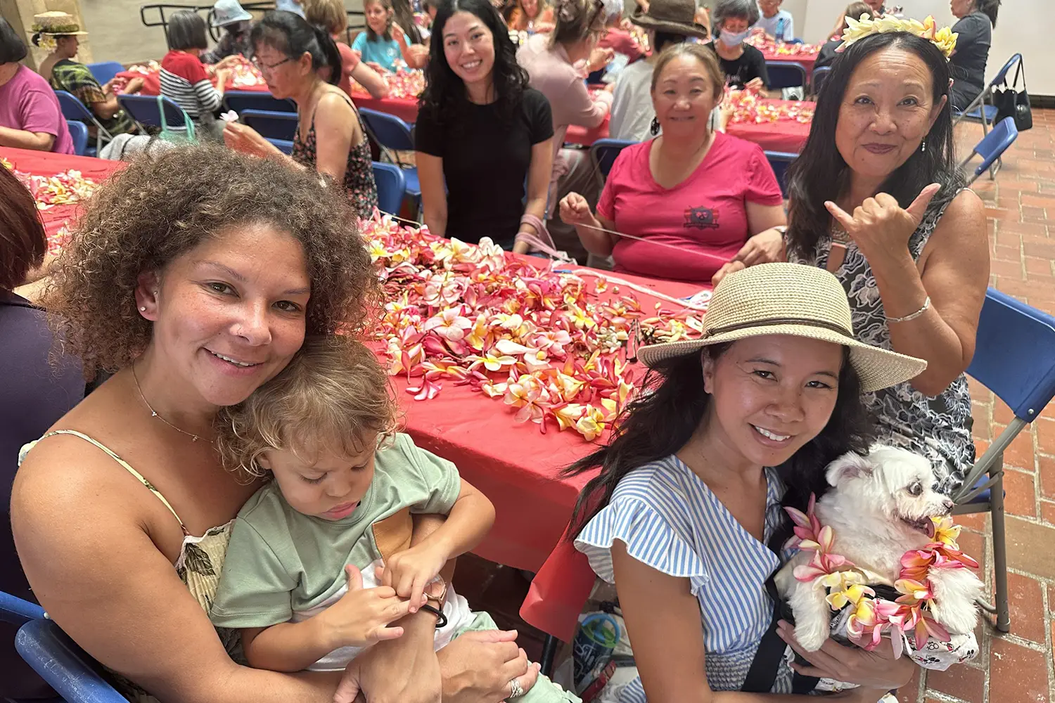 People posing for the camera sitting at a table and participating in a lei making event.