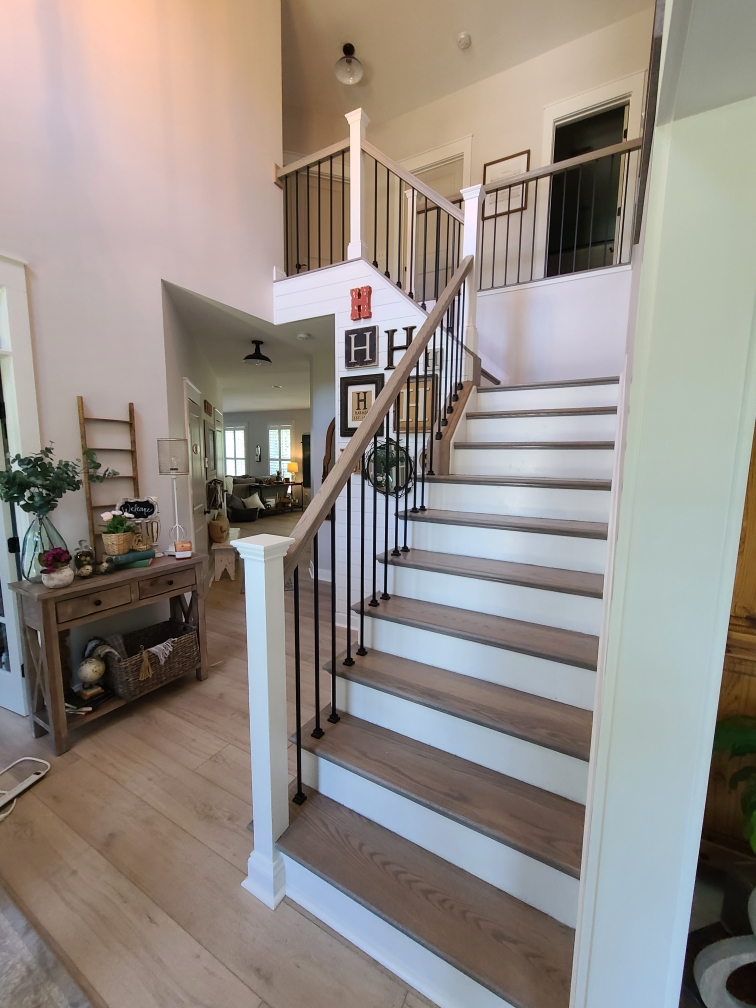 A bright entryway featuring a stylish staircase with white risers, dark treads, and modern black metal balusters.