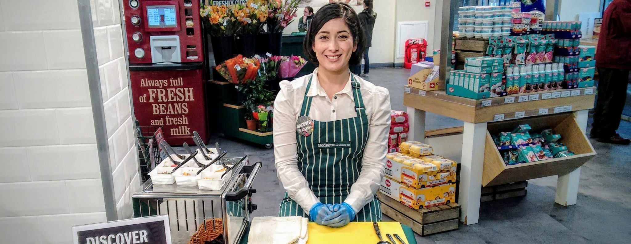Executional gourmet food sampler in an apron serving shoppers in a specialist food store