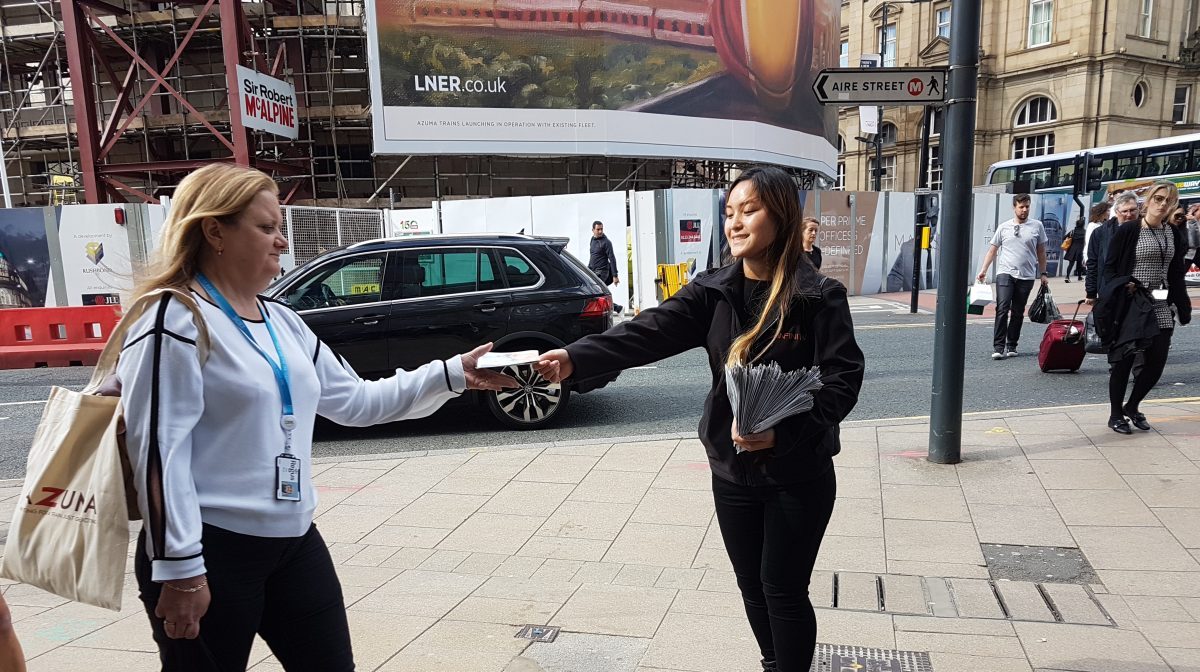 Executional staff member talking to a passer-by on a city street for LNER