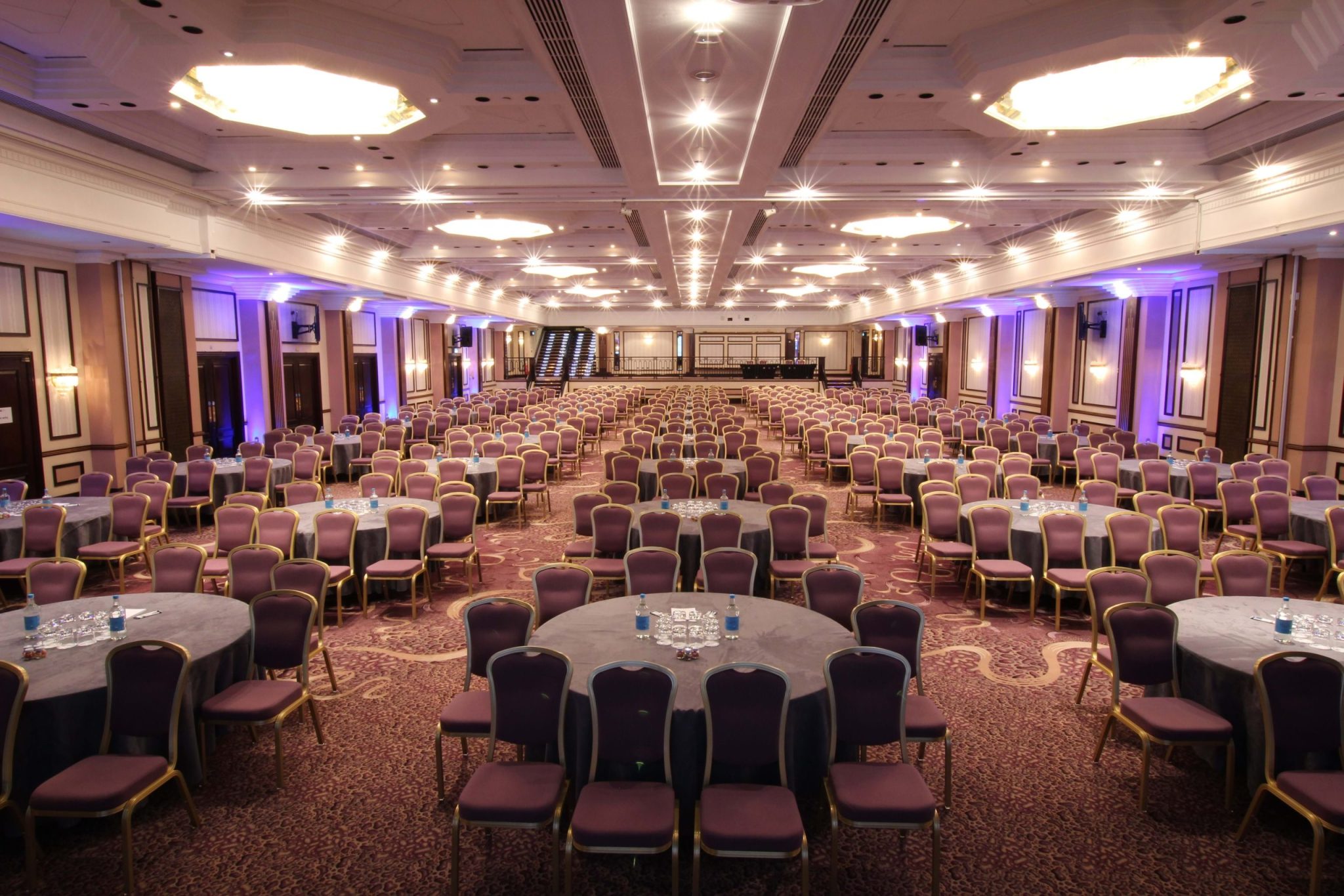 Large conference hall laid out with round tables and chairs under chandeliers