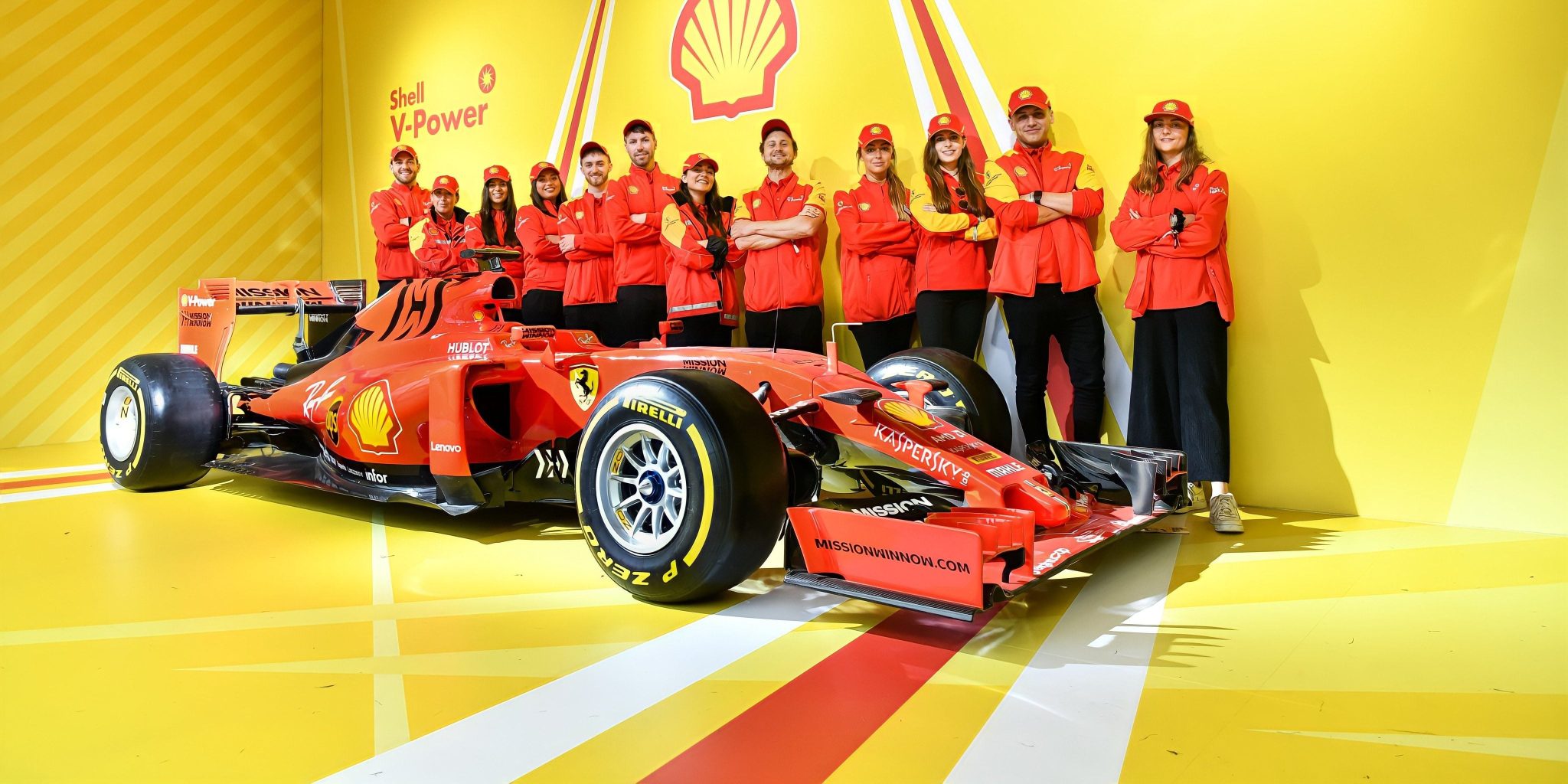 Team in red branded uniforms standing behind a racing car on a bright yellow stand