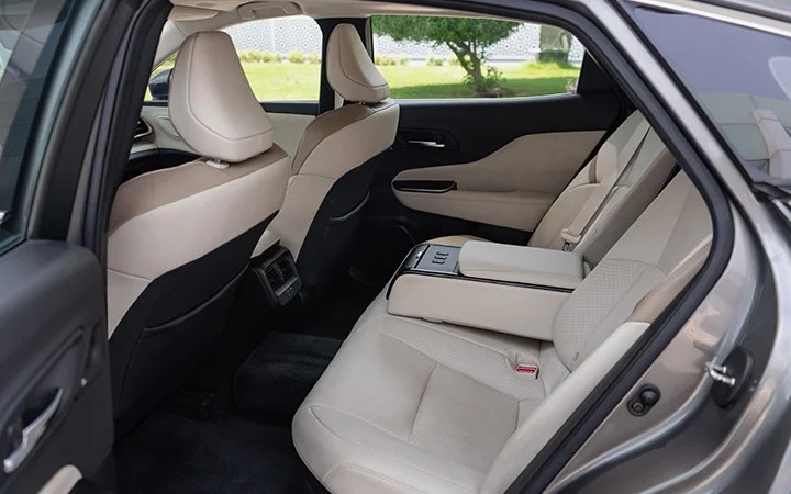 The image shows the backseat interior of a Toyota Camry Qatar with light beige leather seats, a fold-down center armrest, and black carpeting. The doors and front seats are visible, with sunlight coming through the windows.