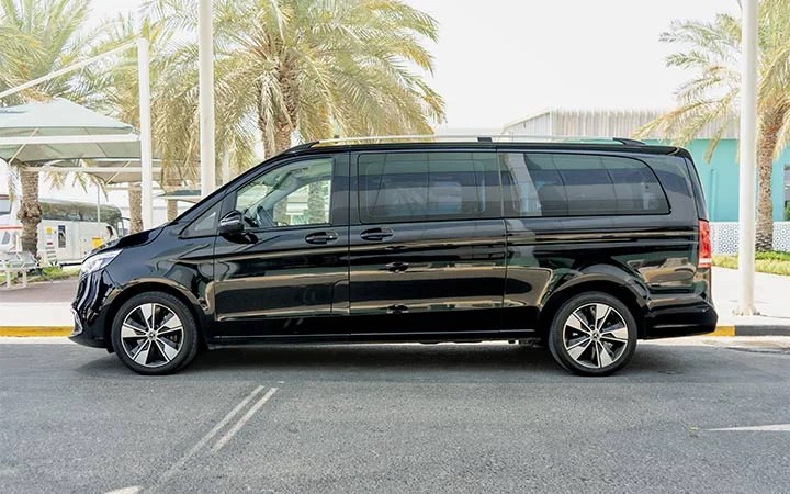 A black Mercedes Viano in Qatar with tinted windows is parked on a street, set against palm trees and modern buildings in the background.