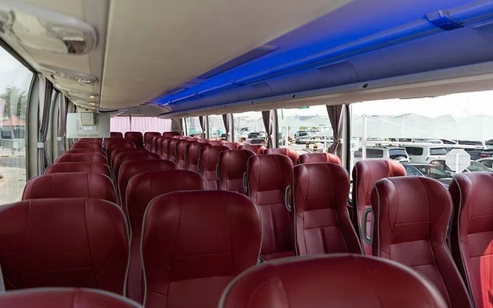 The interior of a Premium Coach Bus Qatar features rows of empty red leather seats, large windows on both sides, and blue accent lighting along the ceiling.