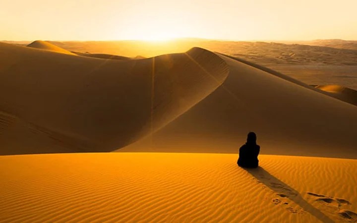 Scenic desert sunset with traveler sitting on sand dune in Qatar
