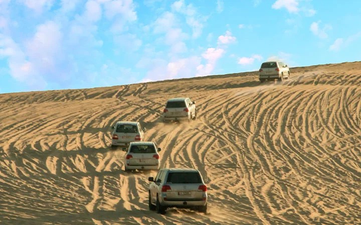 SUVs driving across golden sand dunes during Qatar desert safari adventure
