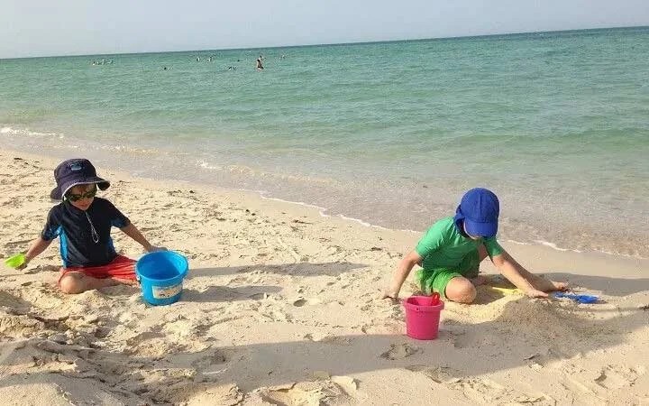 Children playing with sand buckets on Al Maroona Beach Qatar