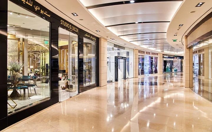 A modern, upscale indoor shopping mall, The Gate Mall Qatar features polished marble floors, curved ceiling lights, and glass storefronts displaying decor and luxury items. The empty corridor gleams with reflections on the shiny floor.
